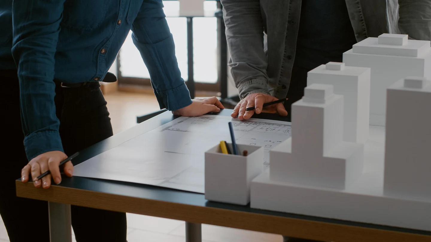 e308ee38-a2eb-437d-950b-ce30e45b1618-close-up-colleagues-working-urban-design-with-blueprints-building-model-team-people-doing-teamwork-construction-layout-designing-architectural-development-project.jpg